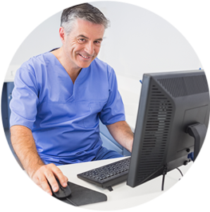 Male doctor sitting at computer desk, smiling.