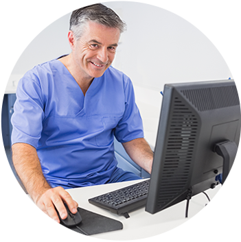 Male doctor sitting at computer desk, smiling.